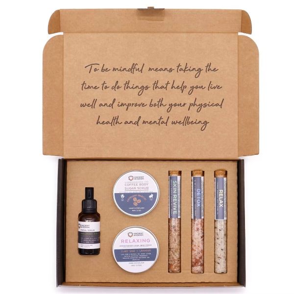 Flat lay of Mindful Moments Self‑Care Kit contents including scrub, cream, bath salts, and serum.