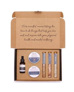 Flat lay of Mindful Moments Self‑Care Kit contents including scrub, cream, bath salts, and serum.