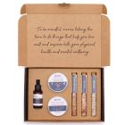 Flat lay of Mindful Moments Self‑Care Kit contents including scrub, cream, bath salts, and serum.