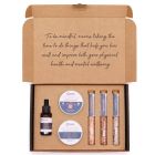Serenity Essential Self‑Care Kit gift box with strawberry scrub, body cream, bath salts, and vitamin C serum arranged together.